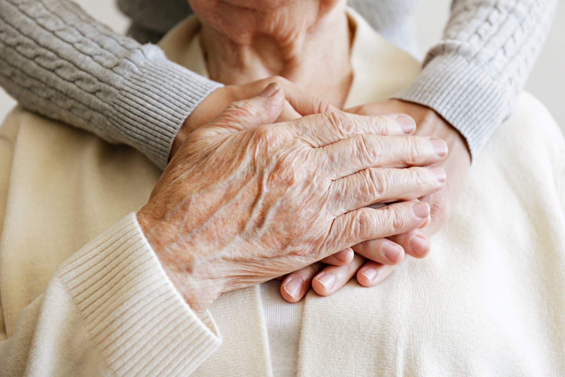 A caregiver's hands resting gently over an elderly woman's hands